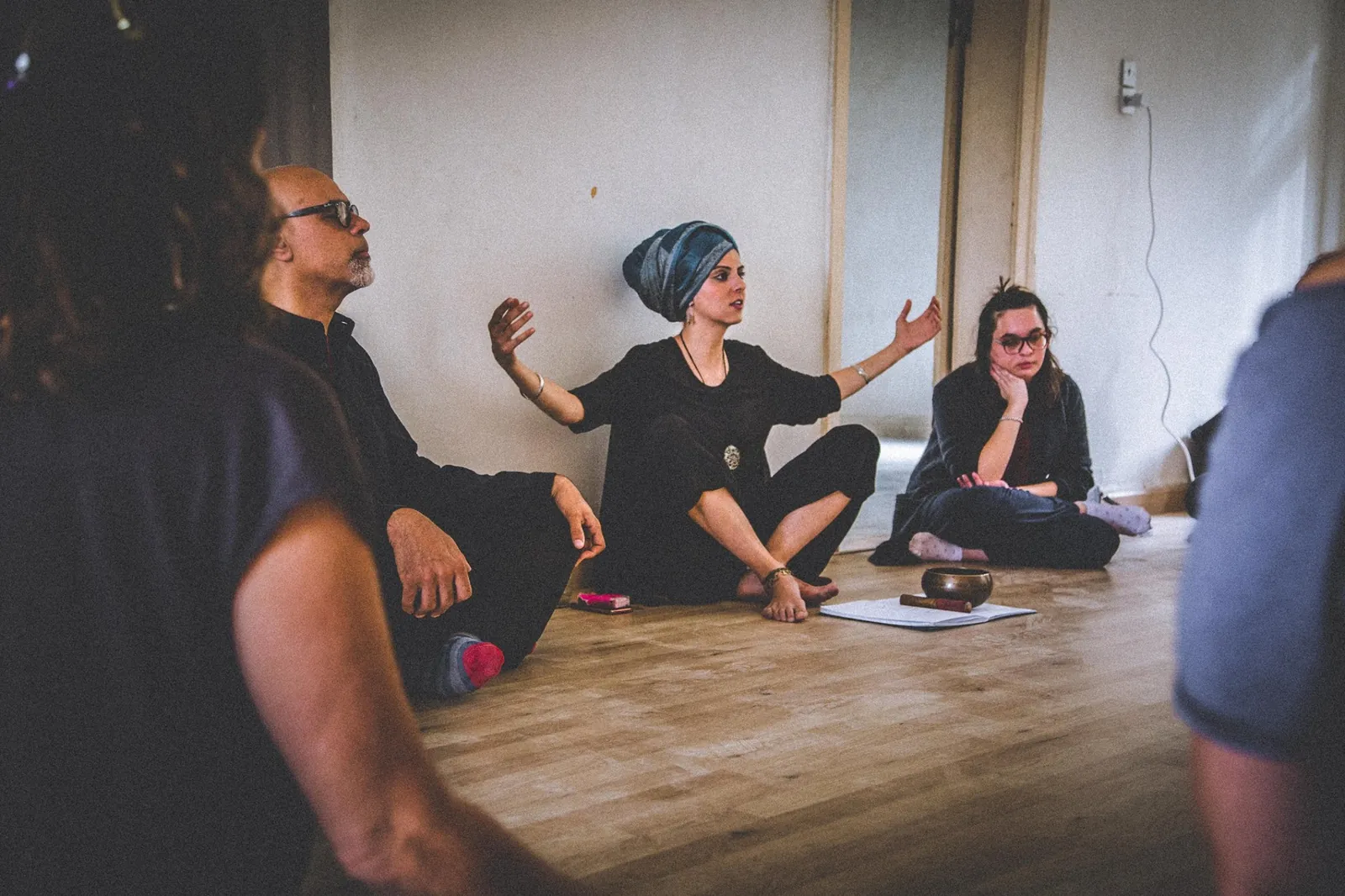 A Wonders of Whirling workshop circle seated on a studio floor, the facilitator speaking with open hands