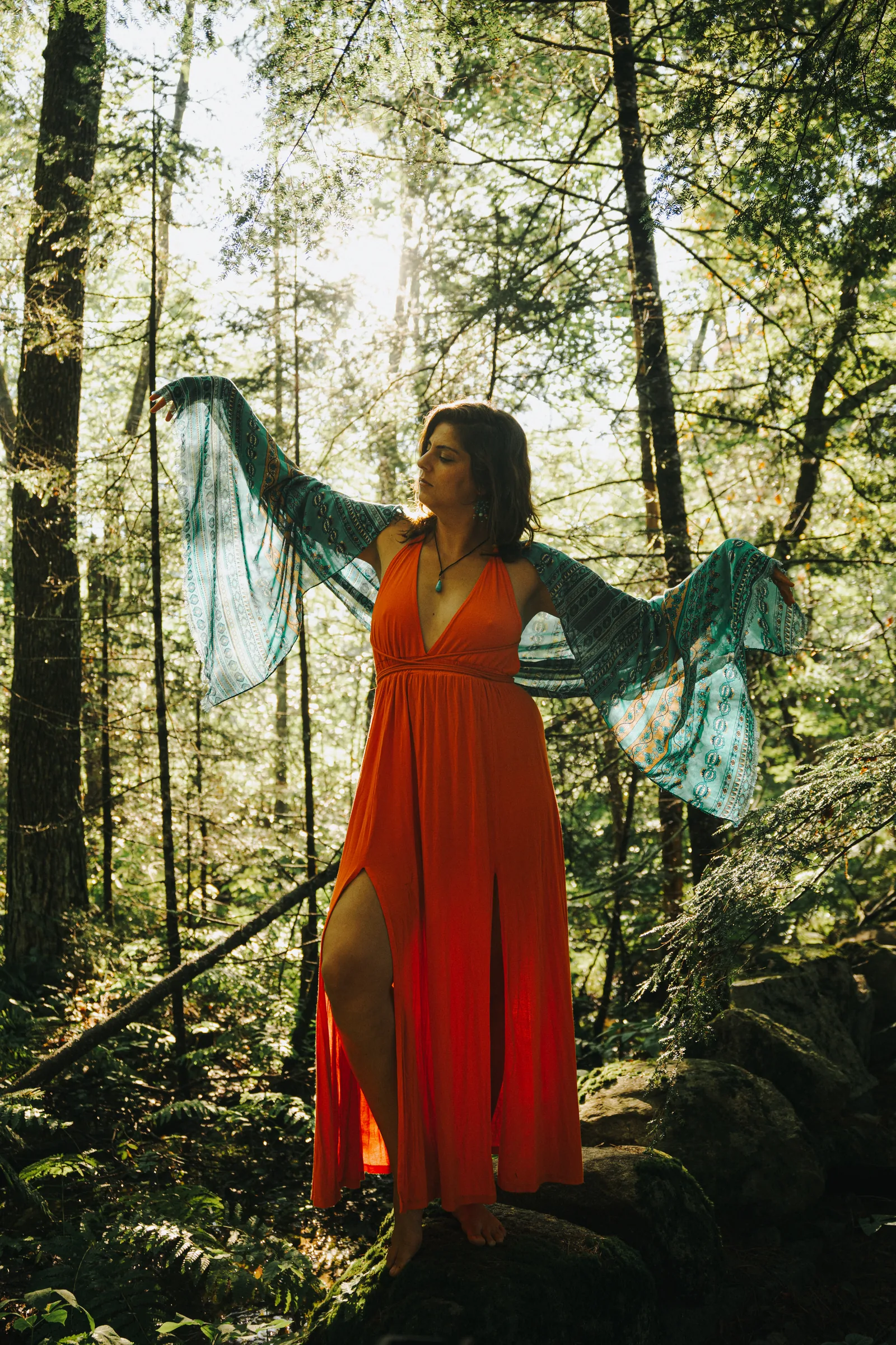 Rawan in an orange dress with teal wings of cloth, in a forest