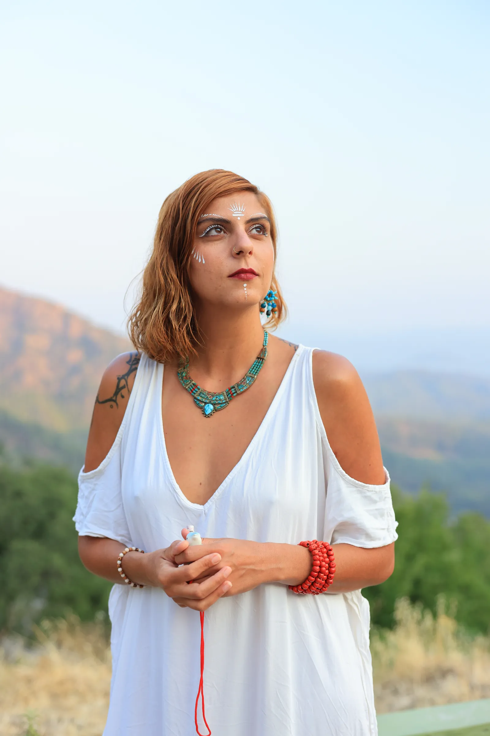 Rawan in white, a turquoise necklace and red beads, the mountains of southern Turkey behind her