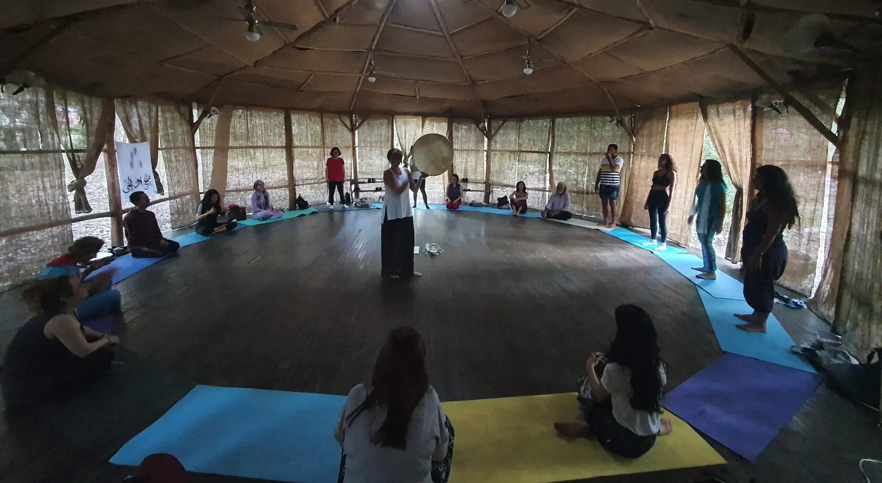 A SoundWork circle in a round wooden hall, participants on mats